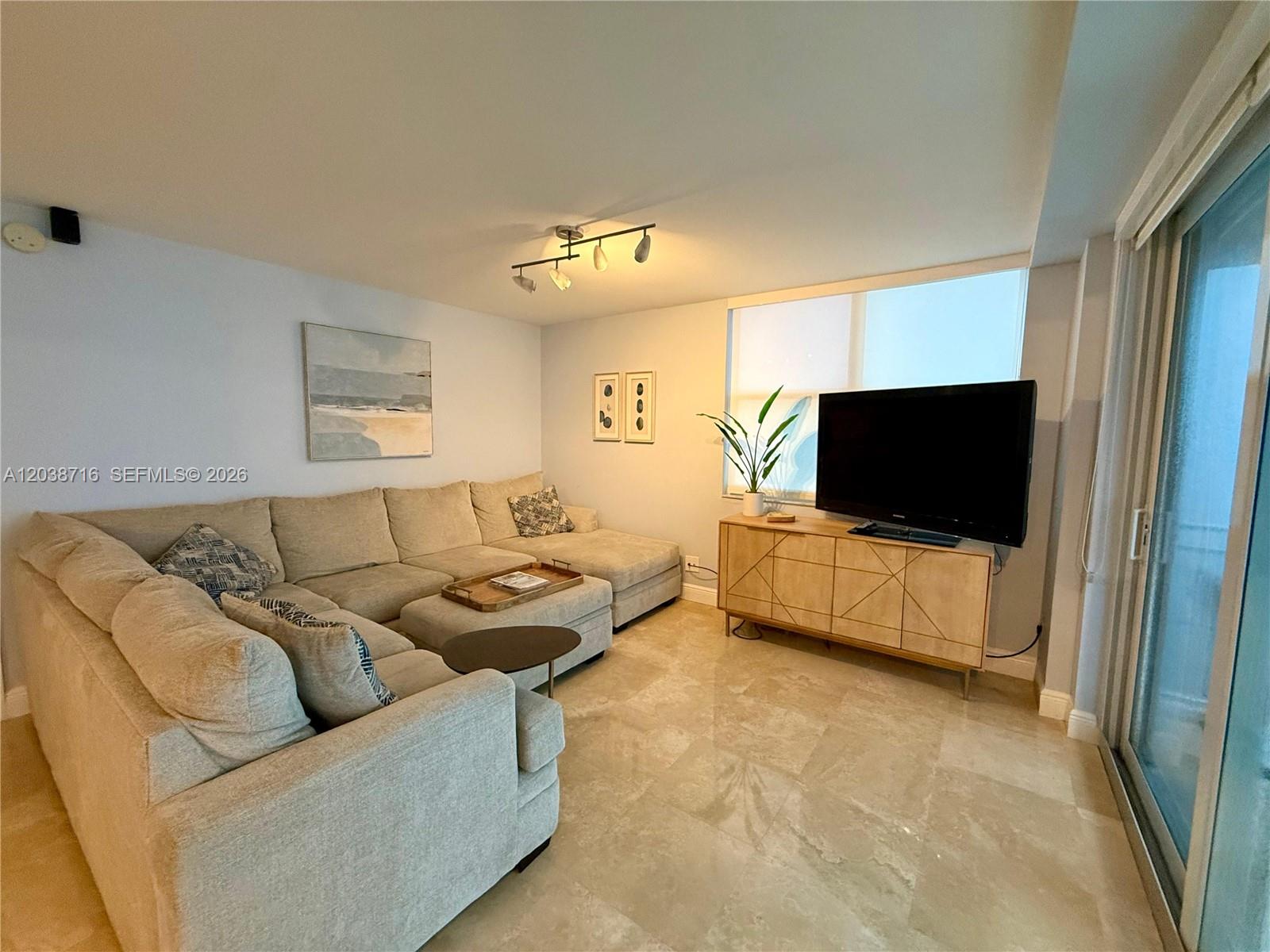 A living room features a large sectional sofa, a television on a wooden console, and tile flooring — 770 Claughton Island Dr # 2016, Miami FL 33131, MIAMI, FL