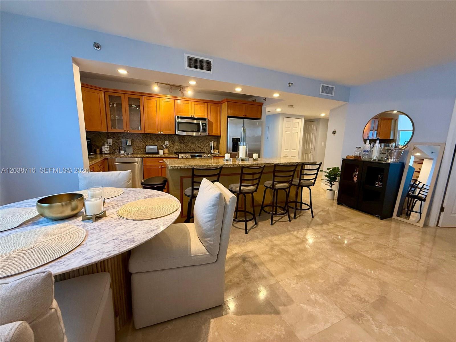 A kitchen with wood cabinets and granite countertops opens to a dining area with tile floors — 770 Claughton Island Dr # 2016, Miami FL 33131, MIAMI, FL