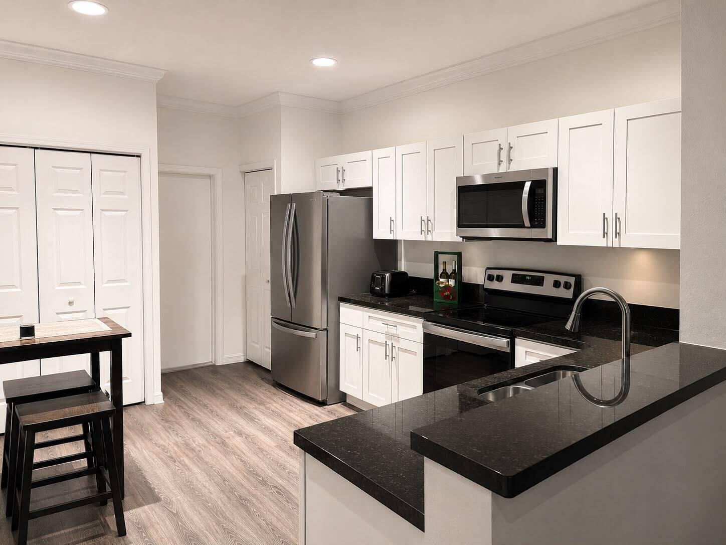 A kitchen with white cabinets, black countertops, stainless steel appliances, and light wood-look flooring — 2166 Hacienda Terrace, Weston FL 33327, WESTON, FL
