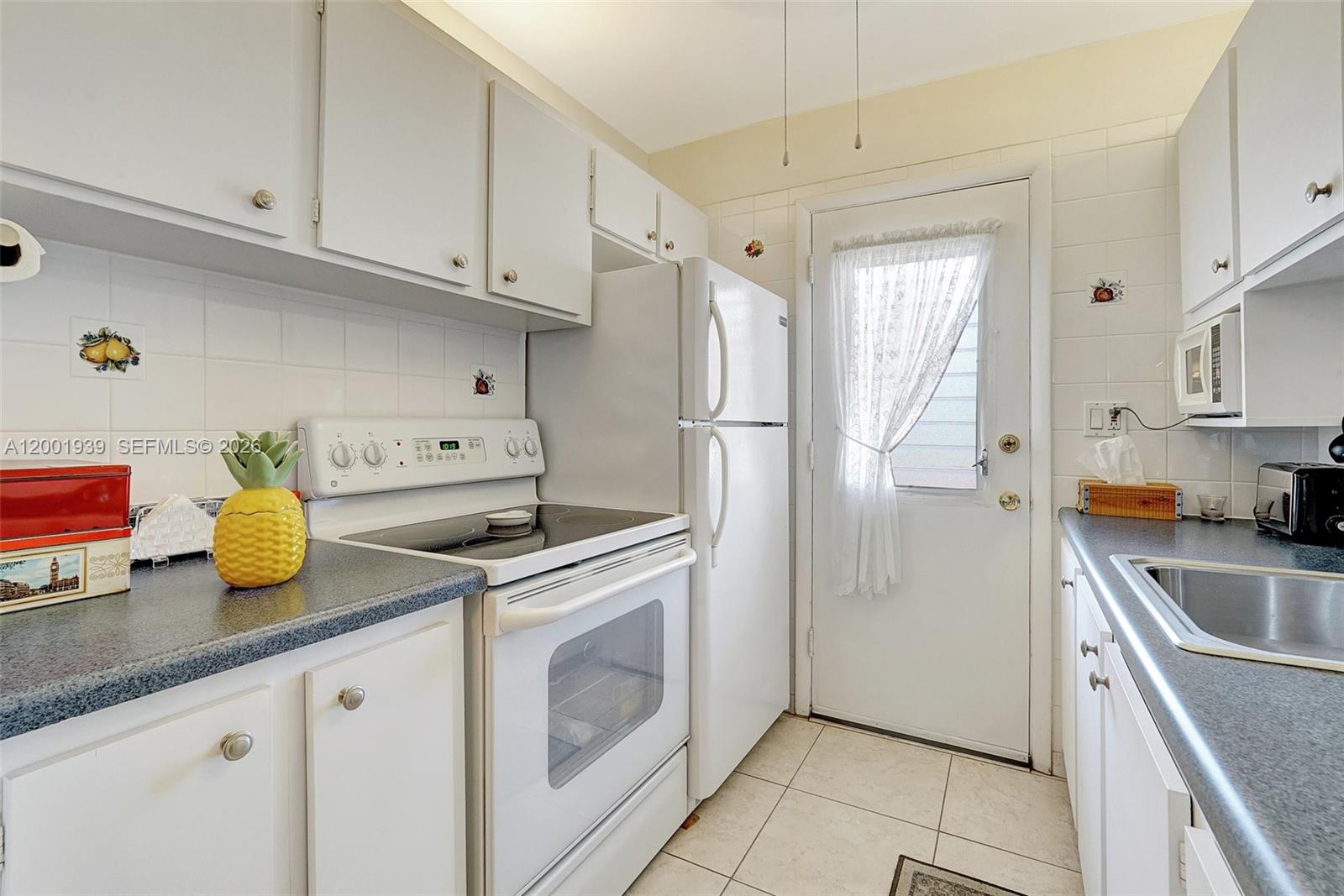 A small kitchen features white cabinets, white appliances, a tiled backsplash, and dark countertops — 16801 NE 13th Ave # 206, Miami FL 33162, MIAMI, FL