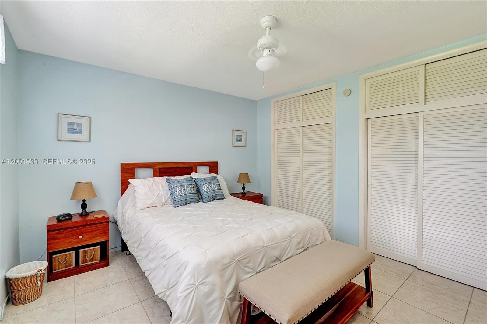A bedroom features a bed with a white comforter, light blue walls, and louvered closets — 16801 NE 13th Ave # 206, Miami FL 33162, MIAMI, FL