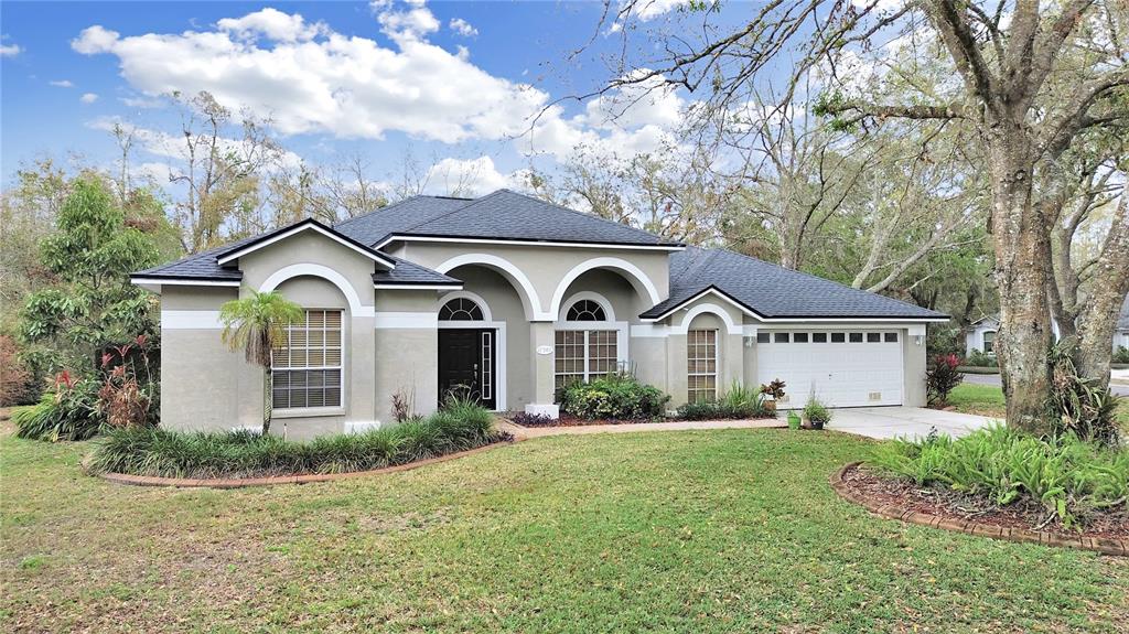 A single-story house with a beige stucco exterior, arched windows, and a two-car garage — 17307 OAK LEDGE DRIVE, LUTZ, FL