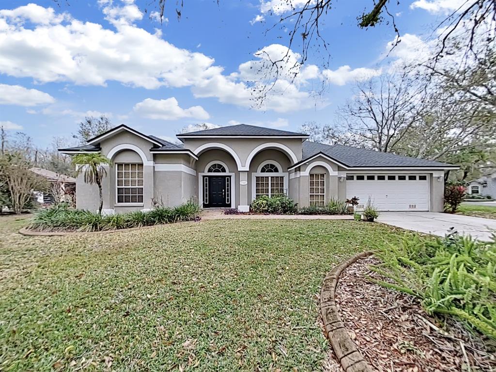 A single-story house with a beige stucco exterior, arched windows, and an attached two-car garage — 17307 OAK LEDGE DRIVE, LUTZ, FL