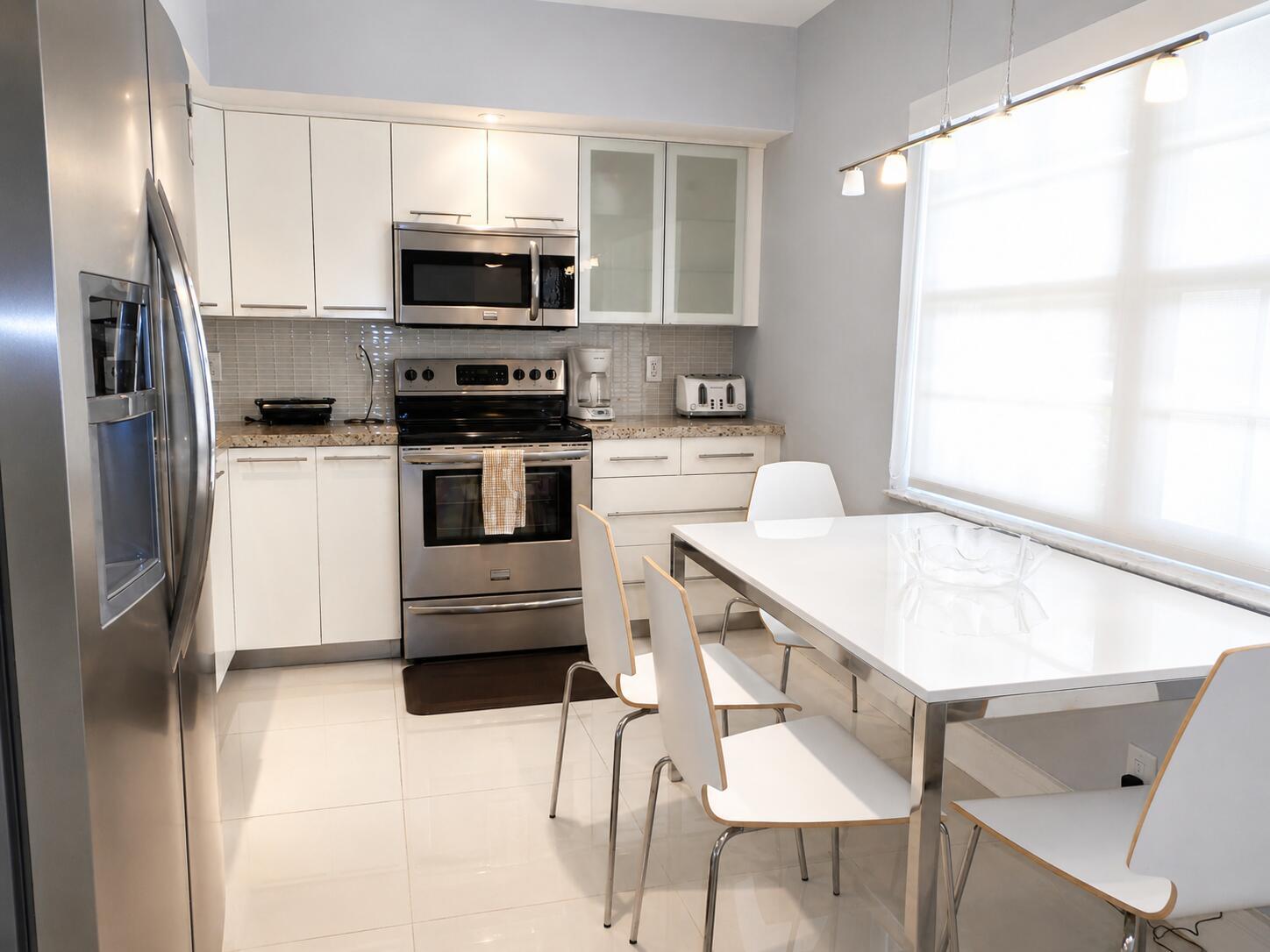 A modern kitchen features white cabinets, stainless steel appliances, and a dining table with chairs — 804 Cypress Boulevard # 104, Pompano Beach FL 33069, POMPANO BEACH, FL