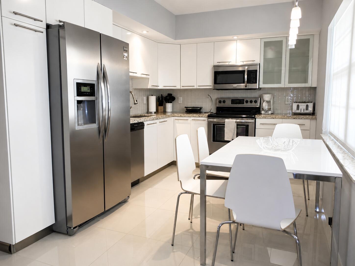 A modern kitchen features white cabinetry, stainless steel appliances, a dining table, and tile flooring — 804 Cypress Boulevard # 104, Pompano Beach FL 33069, POMPANO BEACH, FL
