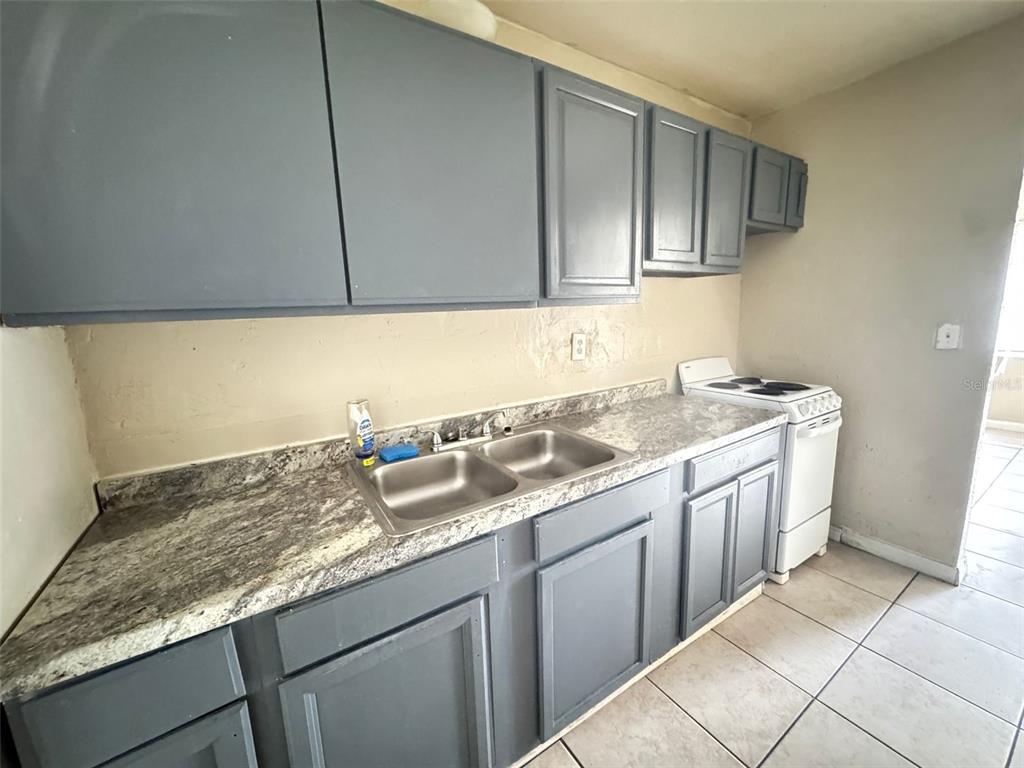 A kitchen features gray cabinets, a double-basin stainless steel sink, and a white electric stove — 1209 CARLSBAD PLACE, ORLANDO, FL