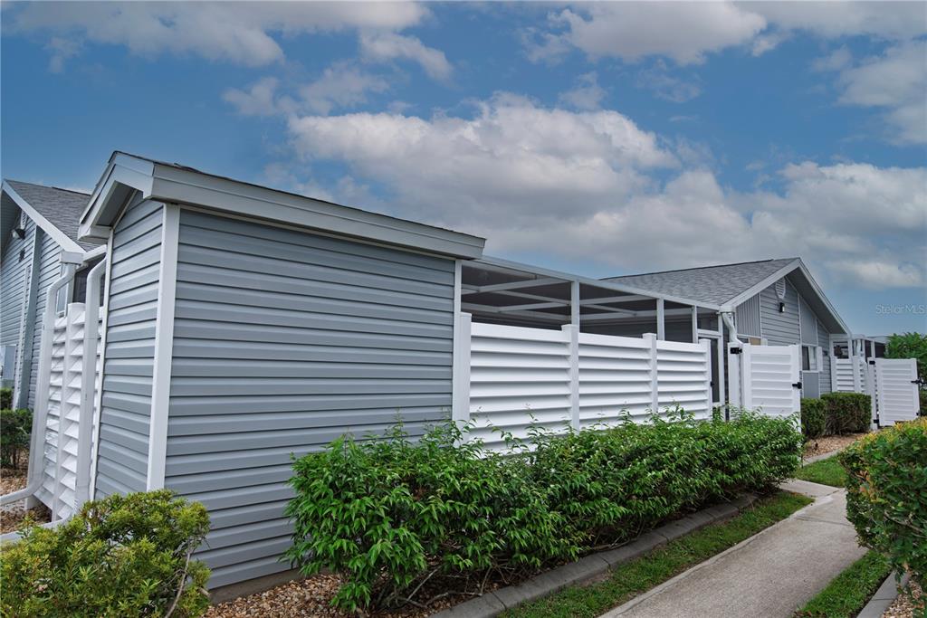 The exterior of a house features gray horizontal siding, a screened-in porch, and white fencing — 3300 LOVELAND BOULEVARD UNIT 2103, PUNTA GORDA, FL