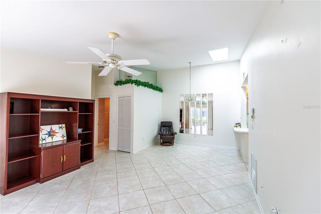 A living room with tile flooring, a ceiling fan, a large bookshelf, and mirrored wall panels — 3300 LOVELAND BOULEVARD UNIT 2103, PUNTA GORDA, FL