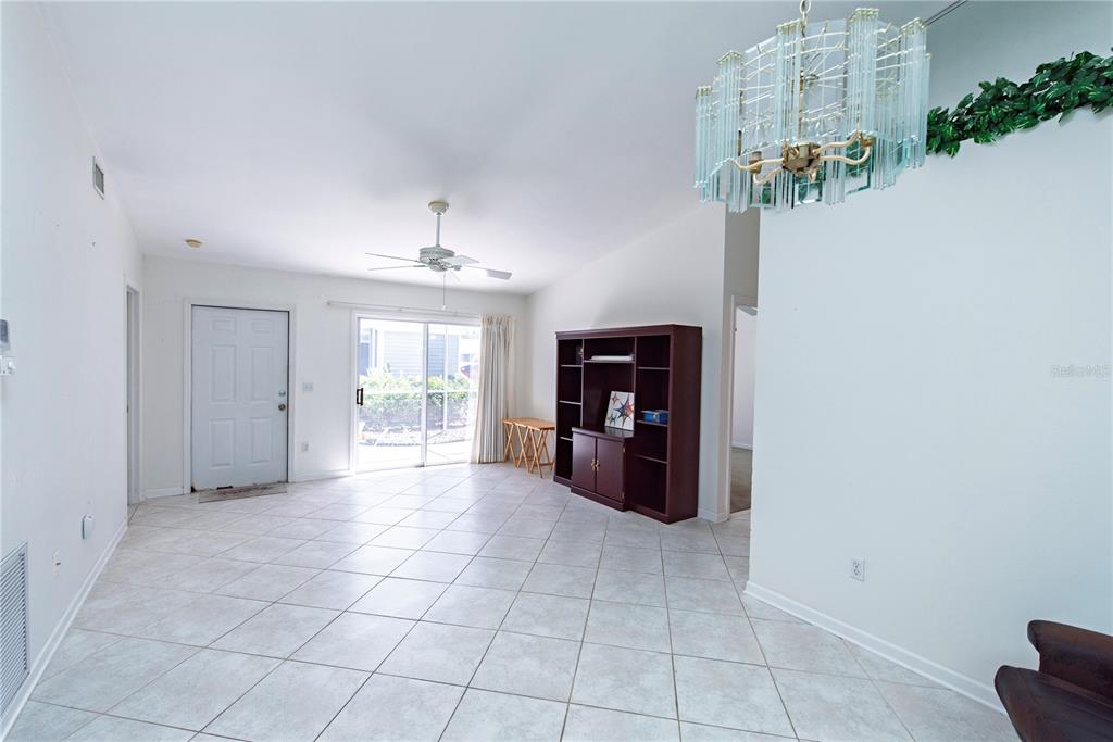 A living room features white tile flooring, a ceiling fan, a chandelier, and a sliding door — 3300 LOVELAND BOULEVARD UNIT 2103, PUNTA GORDA, FL