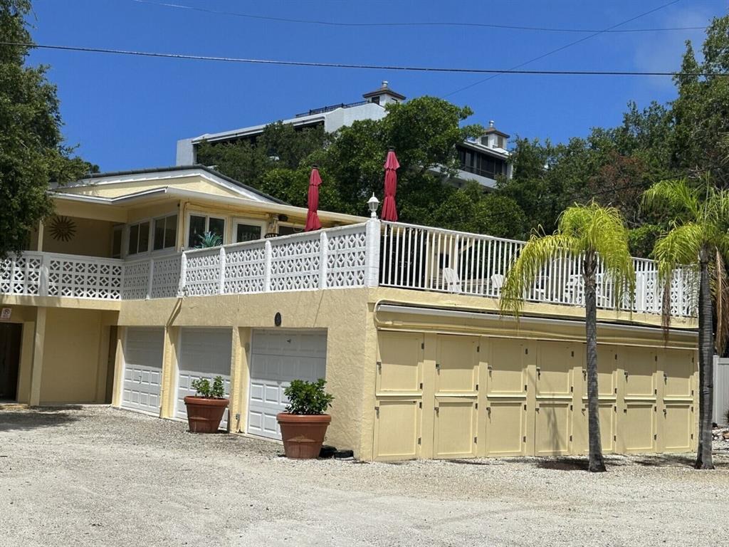 A two-story yellow house features a large elevated deck with white railings and garage doors — 5955 MIDNIGHT PASS ROAD UNIT 21E, SARASOTA, FL