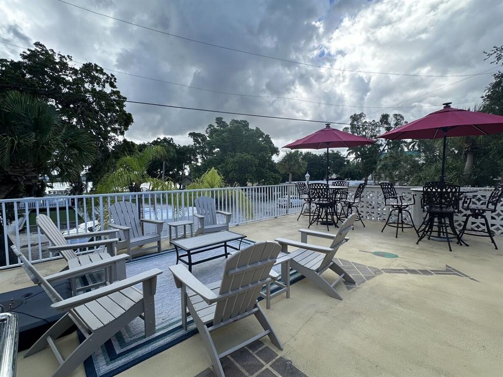 An outdoor patio features gray Adirondack chairs, a small table, and two red umbrellas — 5955 MIDNIGHT PASS ROAD UNIT 21E, SARASOTA, FL