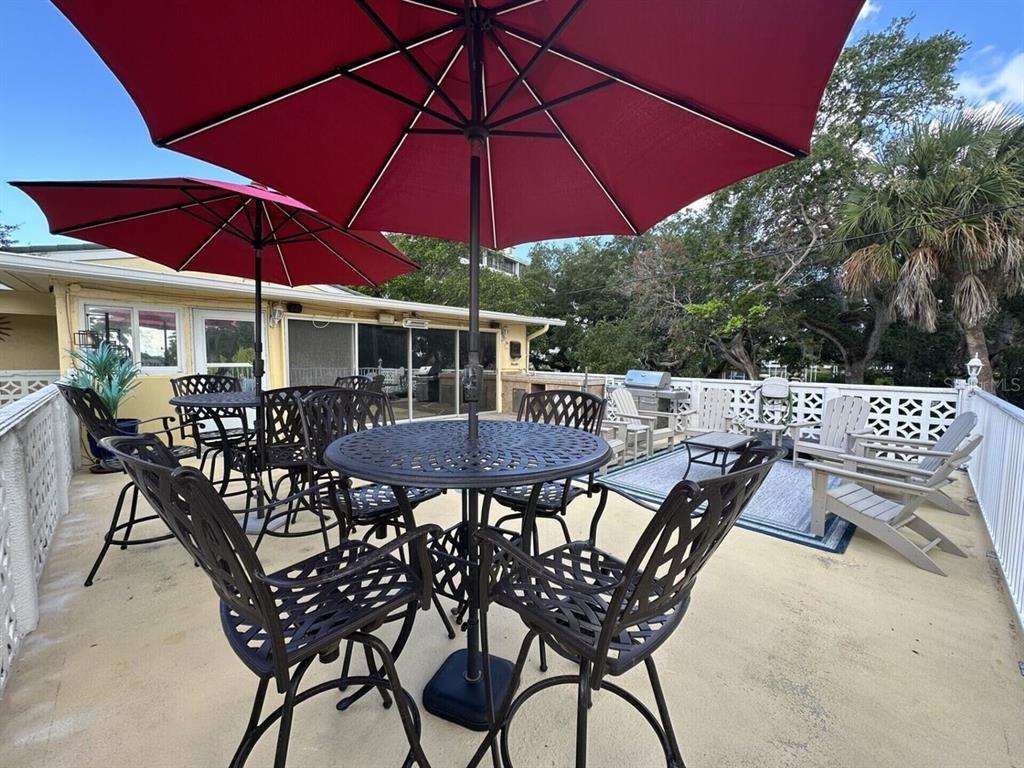 A patio features two red umbrellas, metal dining sets, and lounge chairs on a concrete deck — 5955 MIDNIGHT PASS ROAD UNIT 21E, SARASOTA, FL