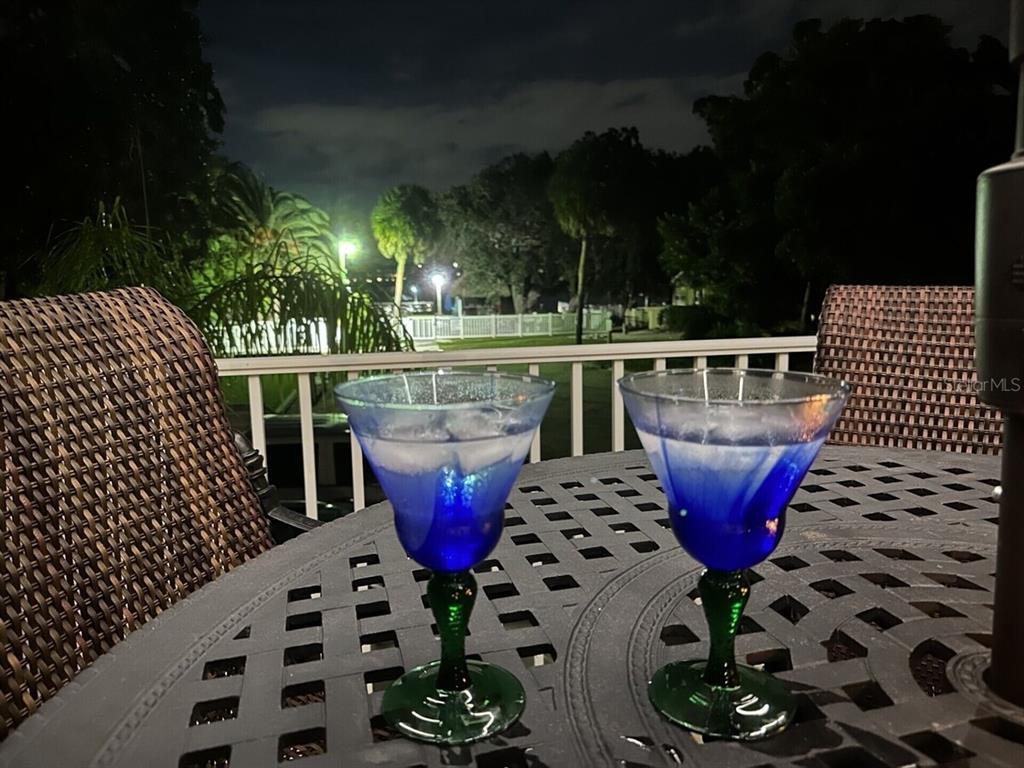Two blue cocktails sit on a patio table at night overlooking a fenced yard — 5955 MIDNIGHT PASS ROAD UNIT 21E, SARASOTA, FL