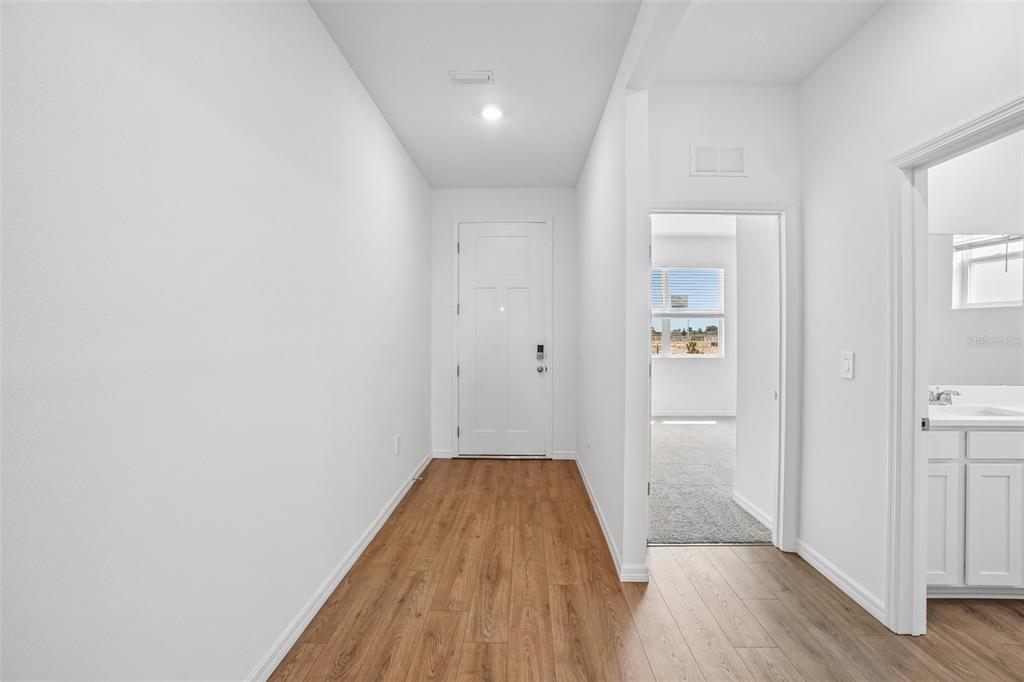 A hallway with wood-look flooring leads to a white front door and an adjacent room — 4672 BARBERRY AVENUE, LAKELAND, FL