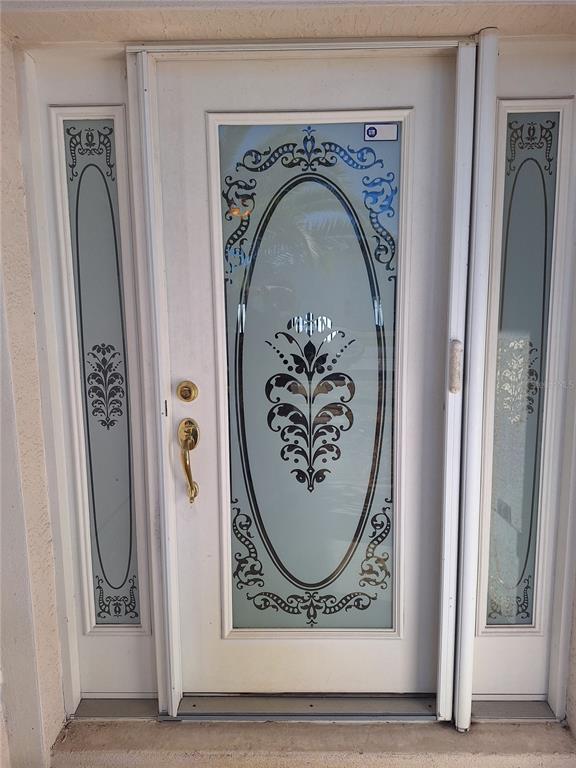 A white front door with a decorative glass oval insert and matching side light panels — 48 WATERS DRIVE, PALM COAST, FL