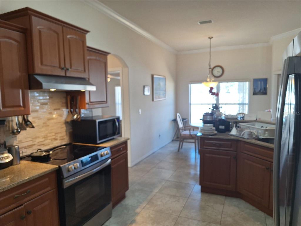A kitchen with wood cabinets, stainless steel appliances, and tile flooring leads to a dining area — 48 WATERS DRIVE, PALM COAST, FL