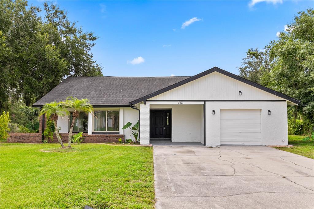 A single-story house with a white stucco exterior, black trim, and an attached one-car garage — 714 DIVOT LANE, POINCIANA, FL