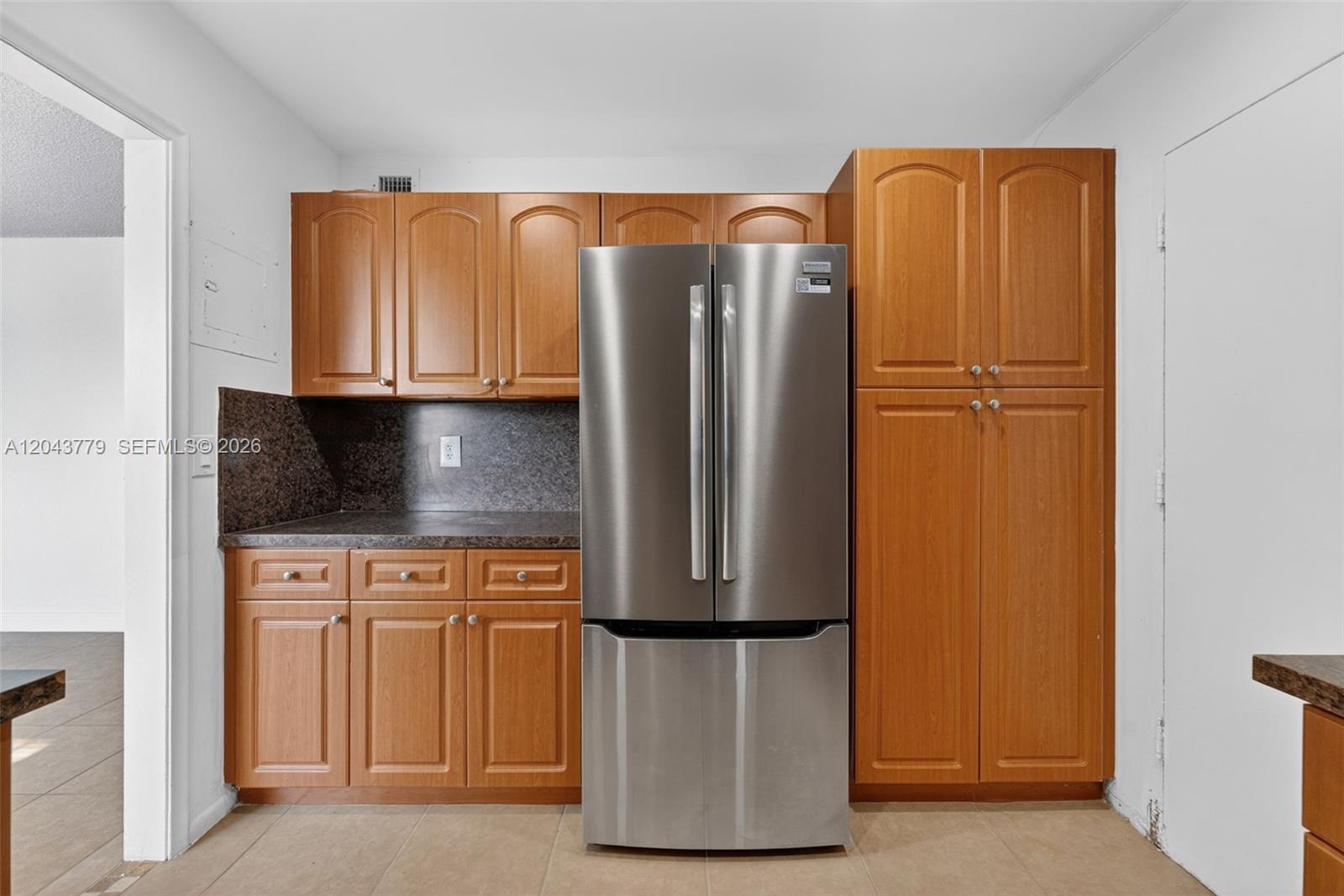 A kitchen features wood cabinets, dark countertops, and a stainless steel refrigerator — 3301 Spanish Moss Ter # 405, Lauderhill FL 33319, LAUDERHILL, FL