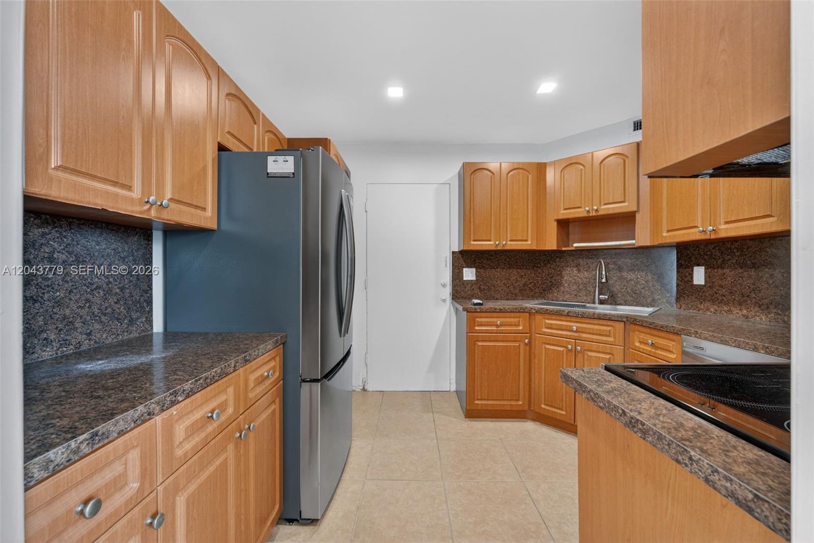 A kitchen features wood cabinets, dark granite countertops, stainless steel appliances, and tile flooring — 3301 Spanish Moss Ter # 405, Lauderhill FL 33319, LAUDERHILL, FL