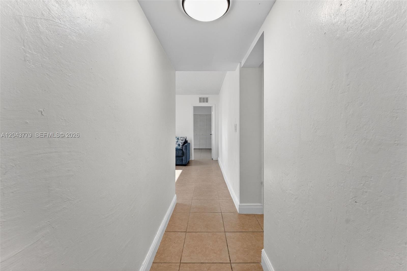 A narrow hallway with white walls and tan tile flooring leads to an open room — 3301 Spanish Moss Ter # 405, Lauderhill FL 33319, LAUDERHILL, FL