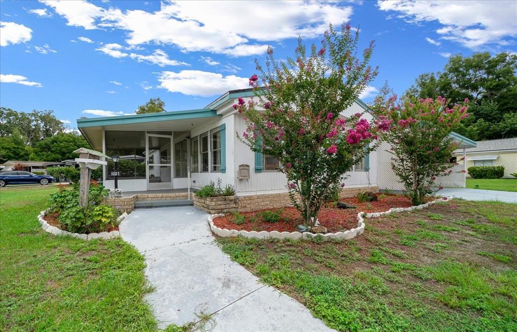 A single-story mobile home with a screened porch, pink flowering trees, and a concrete walkway — 3221 SE 39TH AVENUE, OCALA, FL