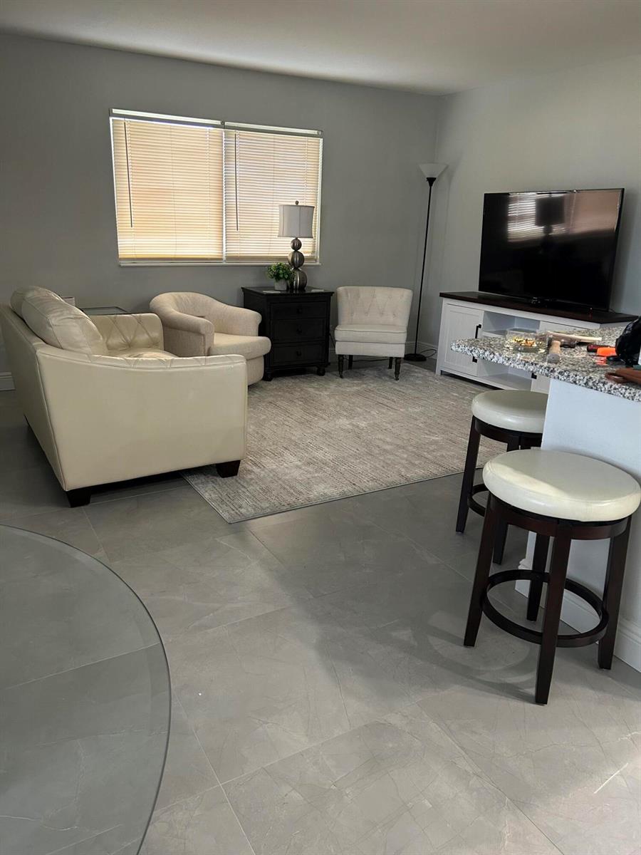 A living room features light tile floors, a neutral area rug, and white furniture — 646 Flanders N, Delray Beach FL 33484, DELRAY BEACH, FL