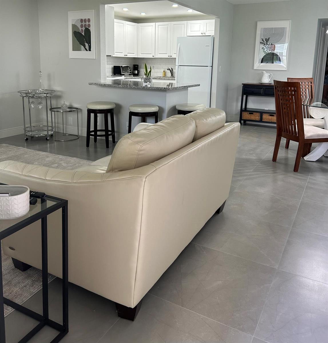 A living room with a beige sofa faces a kitchen with white cabinets and bar stools — 646 Flanders N, Delray Beach FL 33484, DELRAY BEACH, FL
