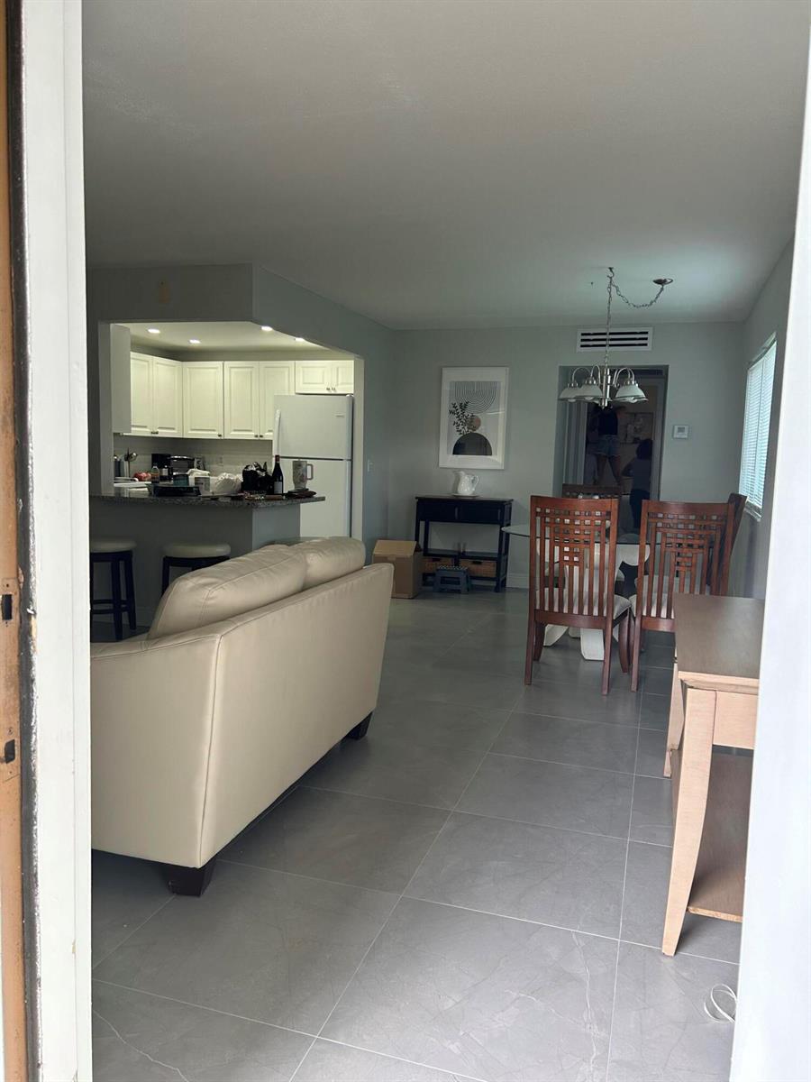 An open-concept living and dining area features light gray tile flooring and white kitchen cabinets — 646 Flanders N, Delray Beach FL 33484, DELRAY BEACH, FL