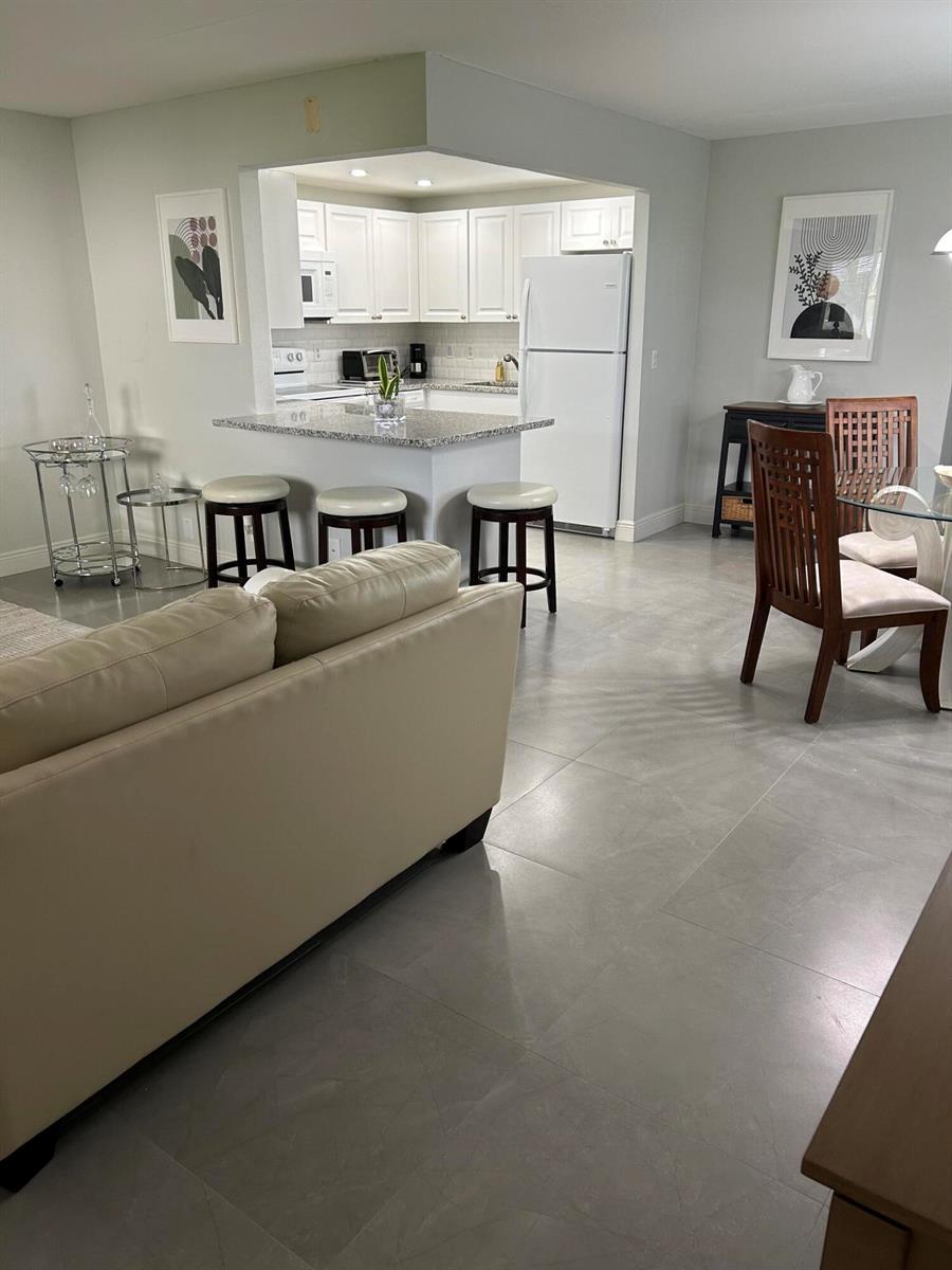 A living room and dining area open to a kitchen with white cabinets and stools — 646 Flanders N, Delray Beach FL 33484, DELRAY BEACH, FL