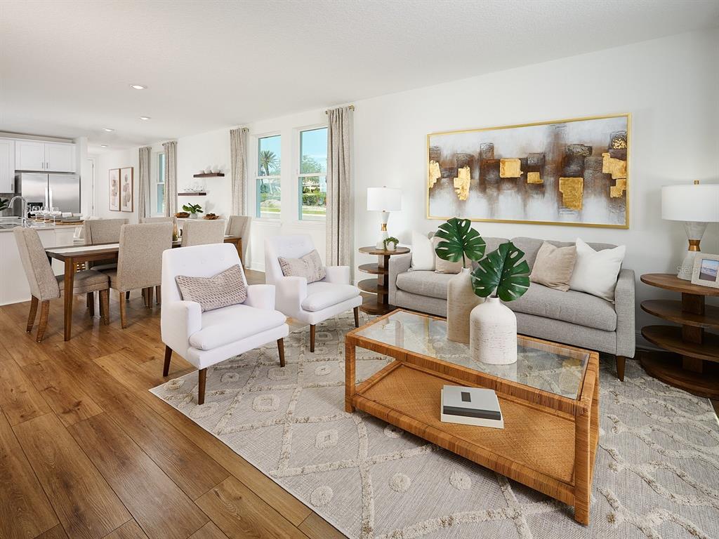 A bright living room features a gray sofa, two white chairs, and a glass coffee table — 3454 MOSCATO DRIVE, BROOKSVILLE, FL