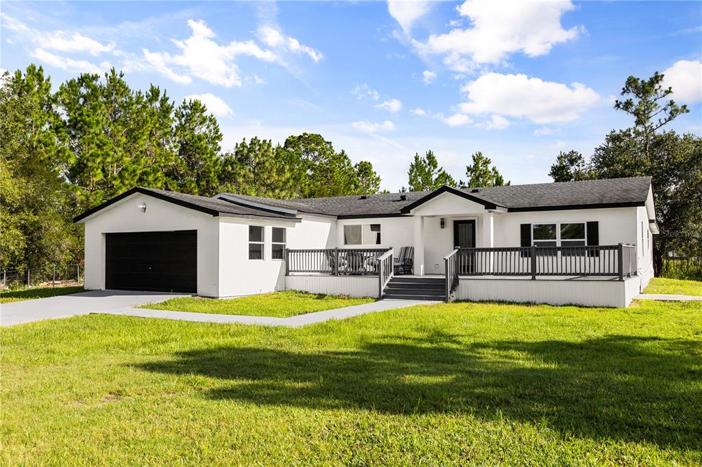 A white single-story house with a black garage door and a large front deck — 19413 OBERLY PARKWAY, ORLANDO, FL