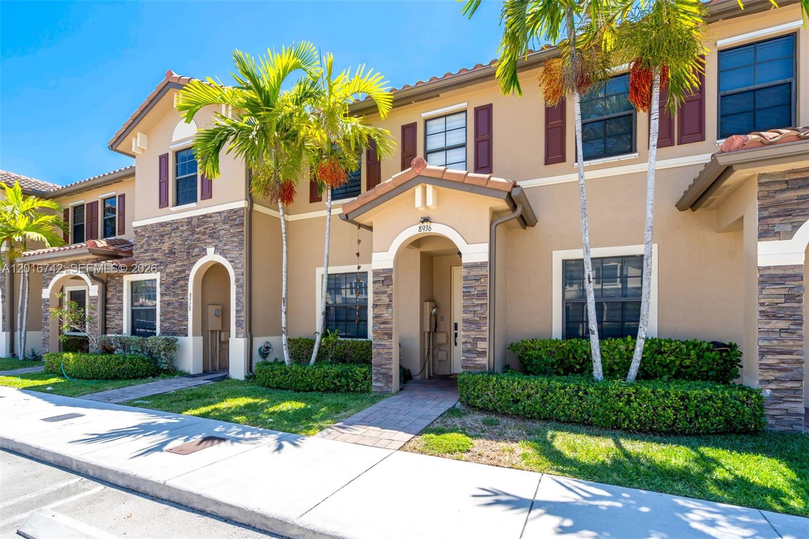 A two-story townhouse exterior features tan stucco walls, stone accents, and palm trees — 8936 W 35th Ln, Hialeah FL 33018, HIALEAH, FL