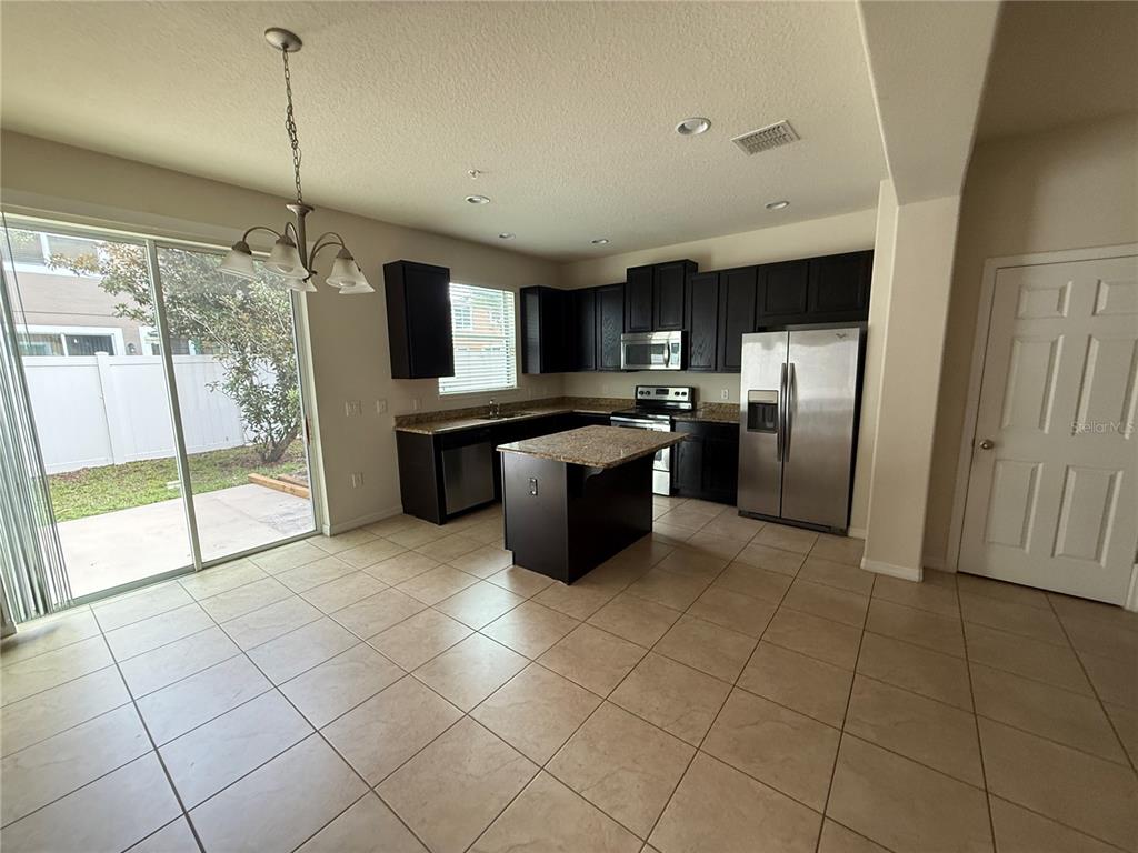 A kitchen features dark wood cabinets, granite countertops, a center island, and tile flooring — 9571 SILVER BUTTONWOOD STREET, ORLANDO, FL