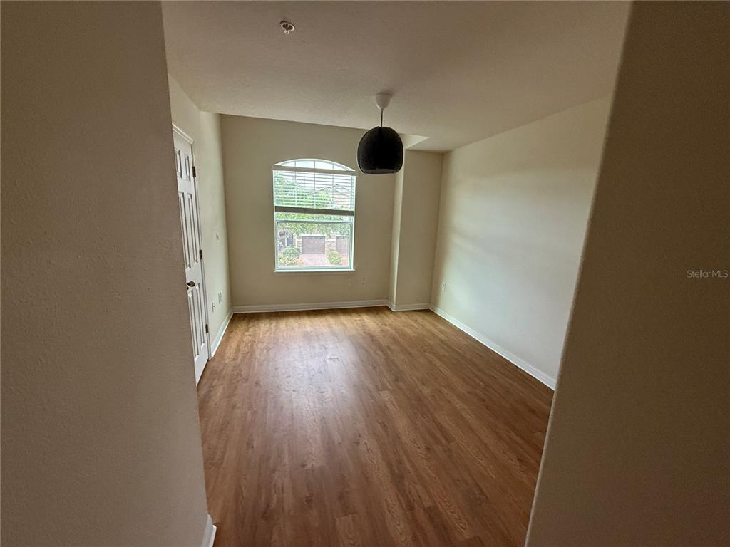 An empty room features light wood-look flooring, a single window, and a dark pendant light — 9571 SILVER BUTTONWOOD STREET, ORLANDO, FL