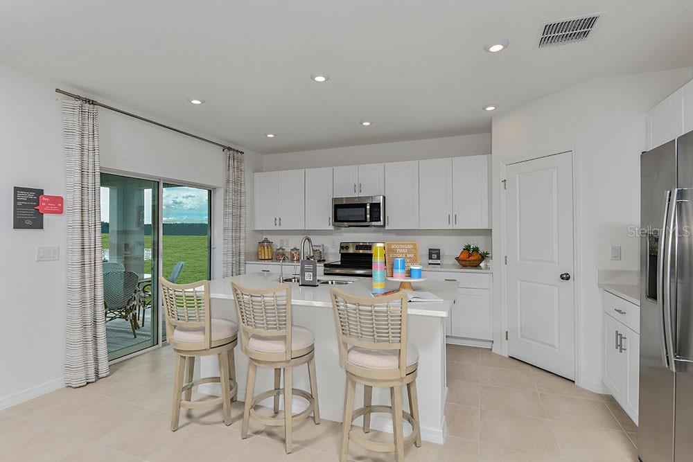 A modern kitchen features white cabinetry, a central island with bar stools, and sliding doors — 6730 EQUINOX LANE, NORTH FORT MYERS, FL