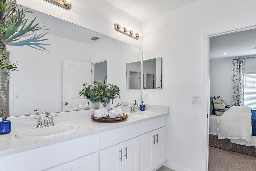 A bright bathroom features a double vanity with white cabinets, quartz countertops, and large mirrors — 6730 EQUINOX LANE, NORTH FORT MYERS, FL