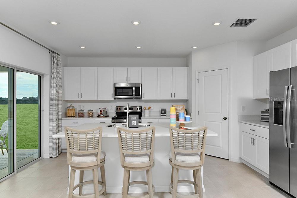A modern kitchen features white cabinetry, a central island with three stools, and a sliding door — 6730 EQUINOX LANE, NORTH FORT MYERS, FL