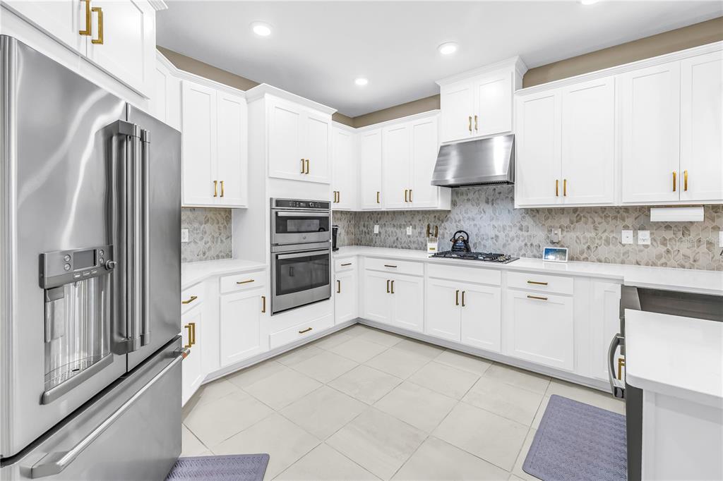 A modern kitchen features white cabinetry, stainless steel appliances, and a patterned tile backsplash — 9240 TEQUILA SUNRISE DRIVE, SARASOTA, FL