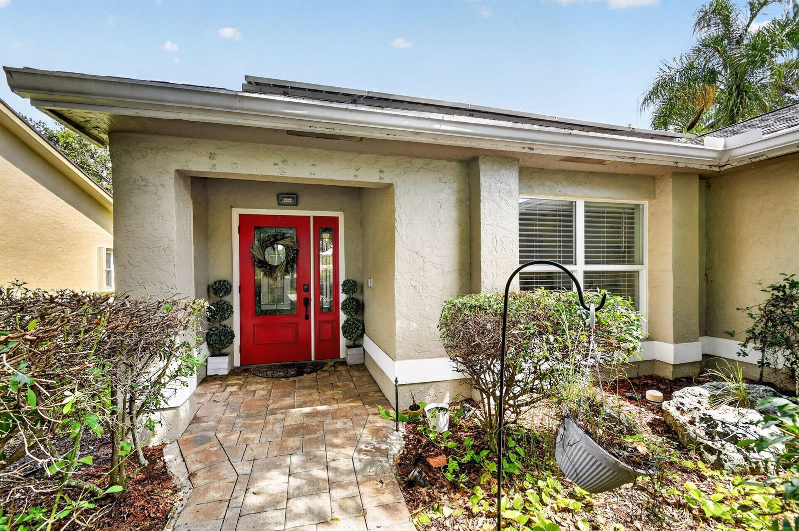 A beige house exterior features a bright red front door and a stone walkway — 4200 Grove Park Lane, Boynton Beach FL 33436, BOYNTON BEACH, FL