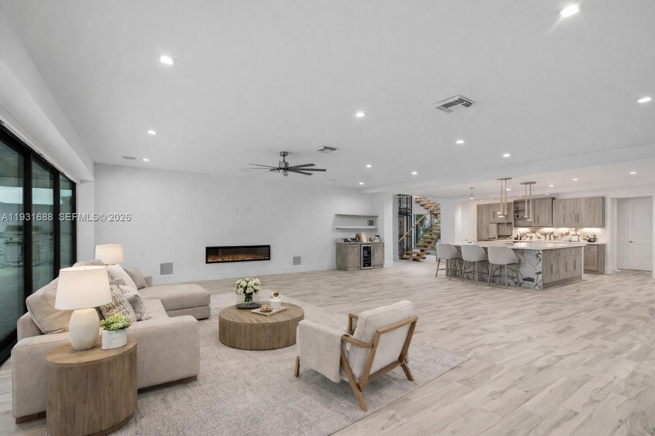 A spacious open-concept living room features a fireplace, a kitchen island, and light wood flooring — 3800 Crayton Road, Naples FL 34103, NAPLES, FL