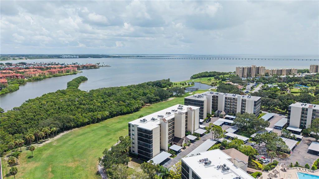 An aerial view shows multi-story apartment buildings situated near a grassy field and a bay — 3300 COVE CAY DRIVE UNIT 7D, CLEARWATER, FL