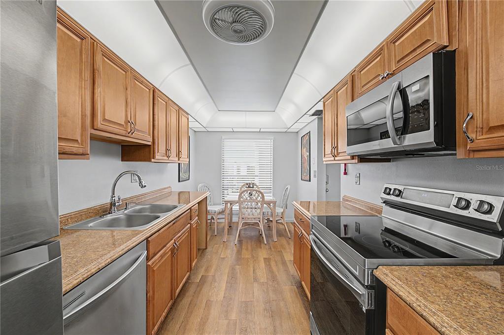 A galley-style kitchen features wood cabinets, granite countertops, stainless steel appliances, and a dining area — 3300 COVE CAY DRIVE UNIT 7D, CLEARWATER, FL