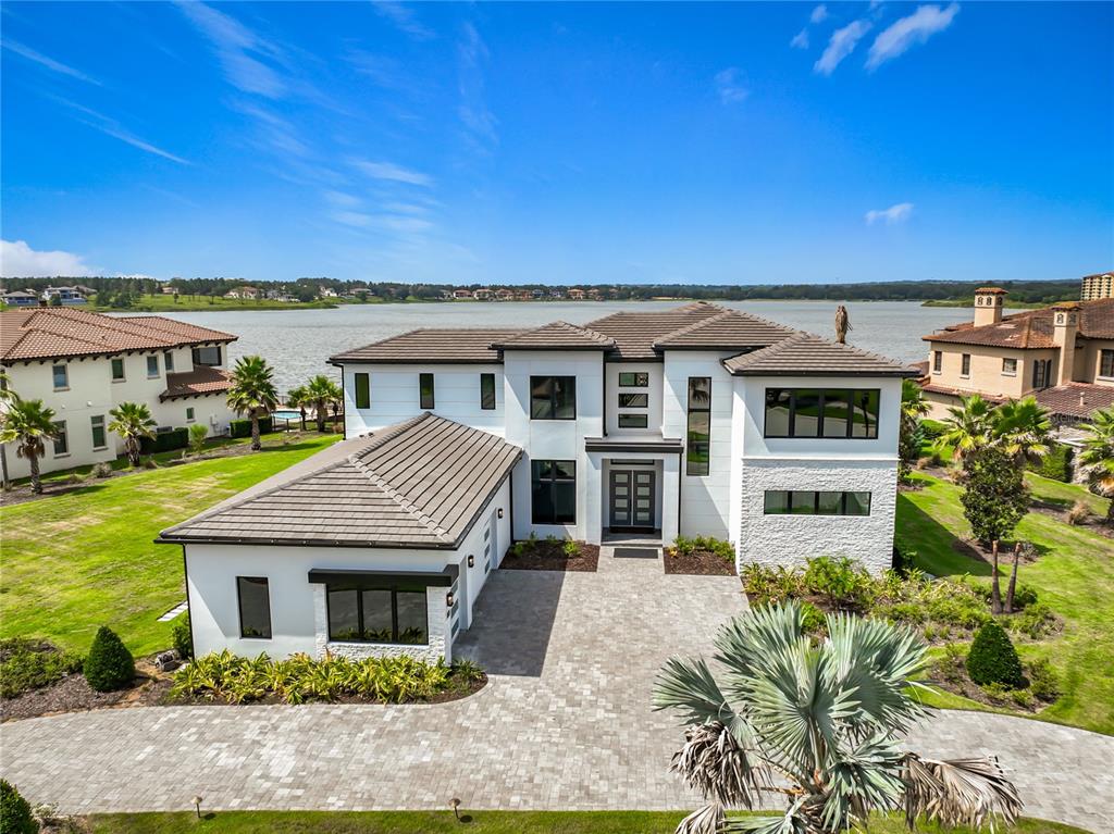 A two-story white modern house with a tiled roof sits beside a large lake — 17300 PESCE LOOP, MONTVERDE, FL