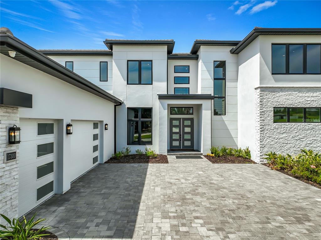 A modern two-story house features white stucco, stone accents, a paved driveway, and dark-framed windows — 17300 PESCE LOOP, MONTVERDE, FL