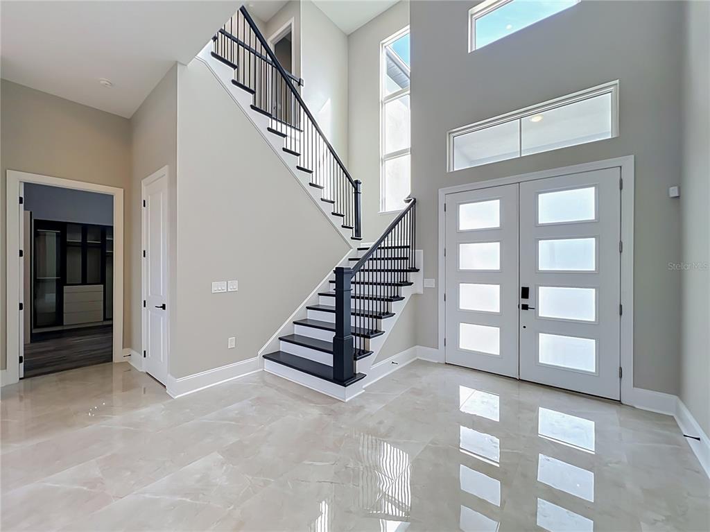 A bright foyer features a staircase with black railings, light tile flooring, and double doors — 17300 PESCE LOOP, MONTVERDE, FL