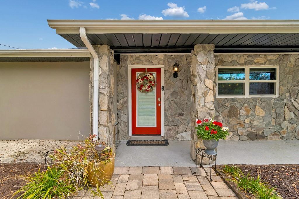 A stone-faced house exterior features a bright red front door and a paved walkway — 1611 SUNNYHILLS DRIVE, BRANDON, FL