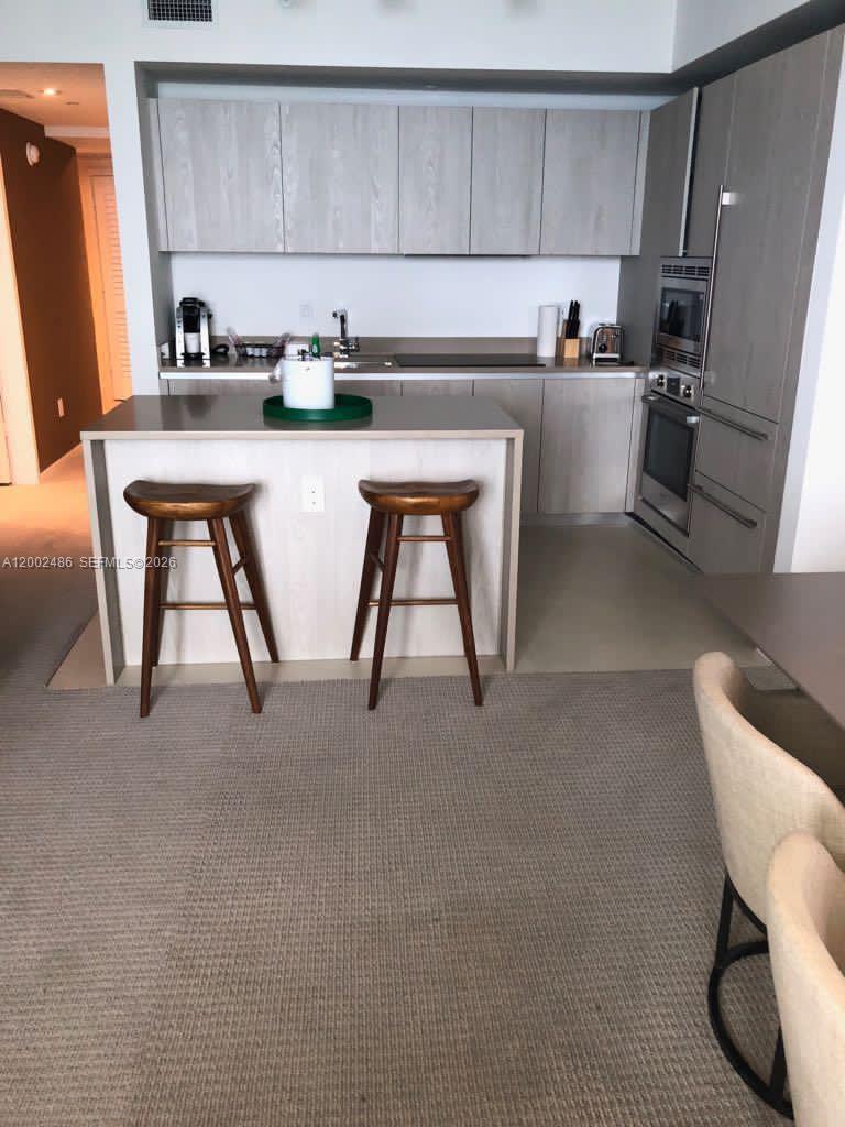 A modern kitchen features light wood cabinetry, a central island with two stools, and appliances — 4111 S Ocean Dr # 1002, Hollywood FL 33019, HOLLYWOOD, FL