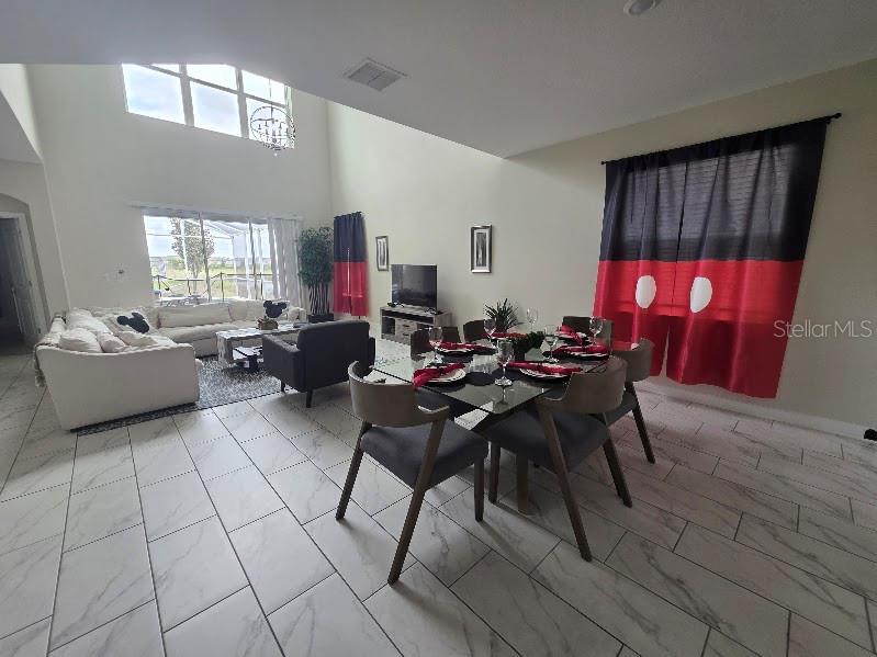 A bright open-concept living and dining area features white tile floors and Mickey Mouse-themed curtains — 651 DROP SHOT DRIVE, DAVENPORT, FL