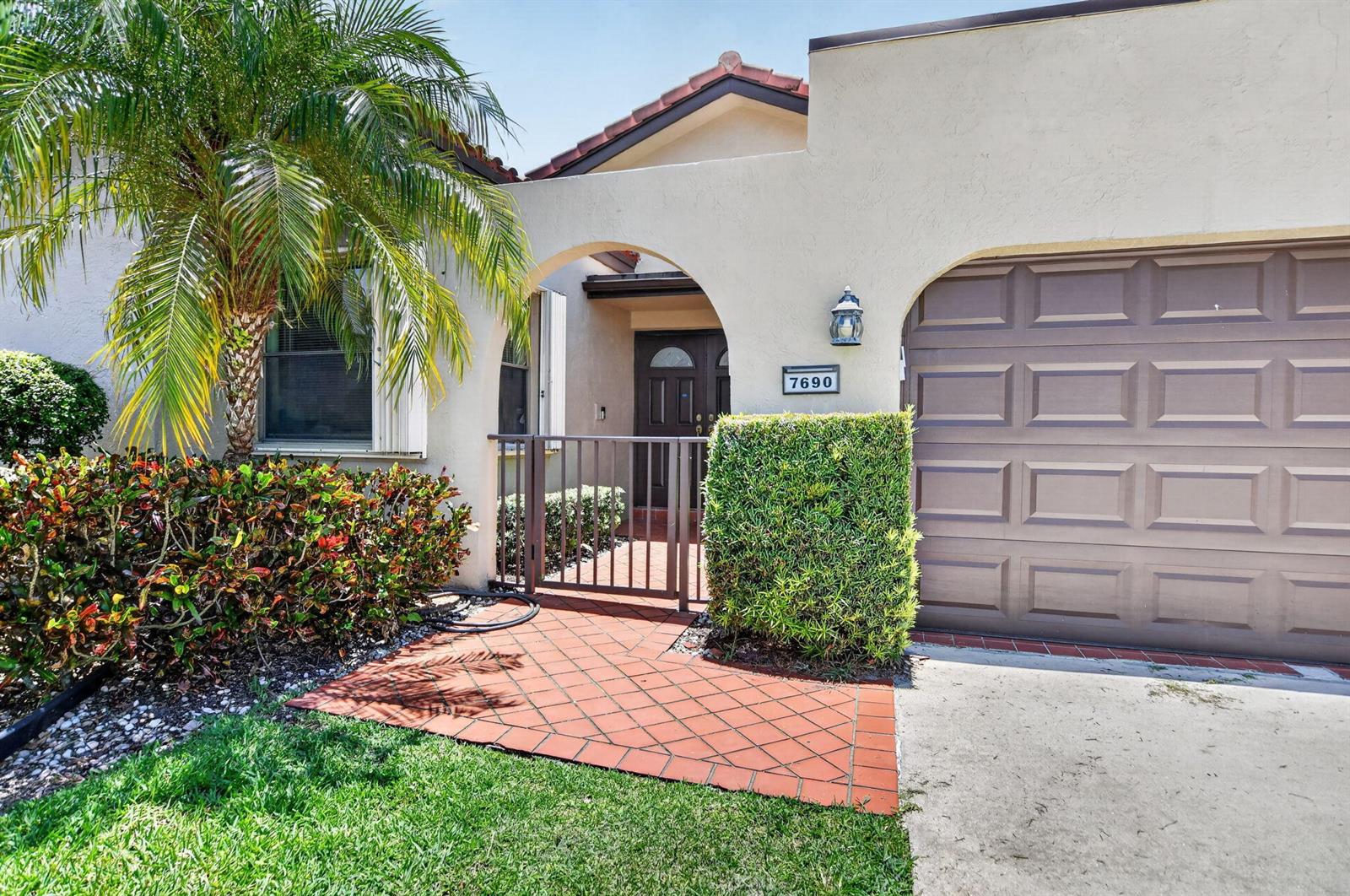 A house exterior features a brown garage door, a gated courtyard, and a palm tree — 7690 Solimar Circle, Boca Raton FL 33433, BOCA RATON, FL