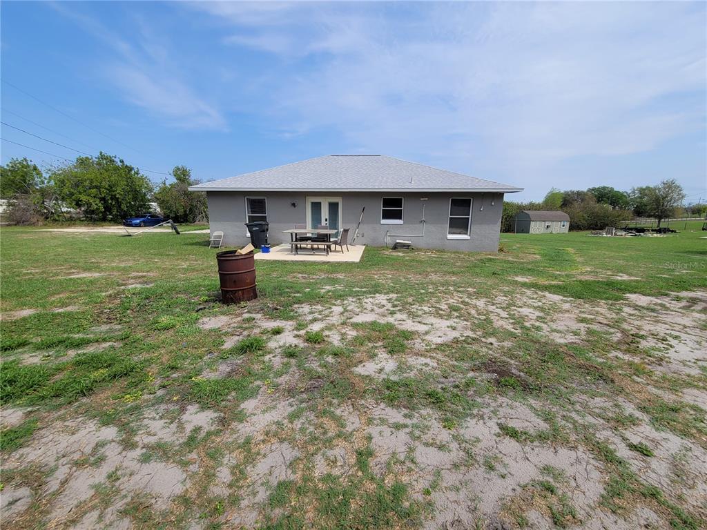 The back exterior of a gray house features a small patio, a table, and chairs — 425 STOKES RD, LAKE WALES, FL